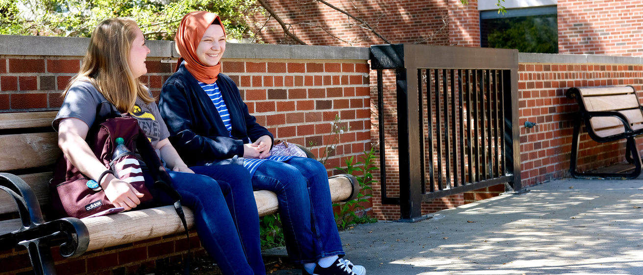 International Studies students laughing together on a campus bench.